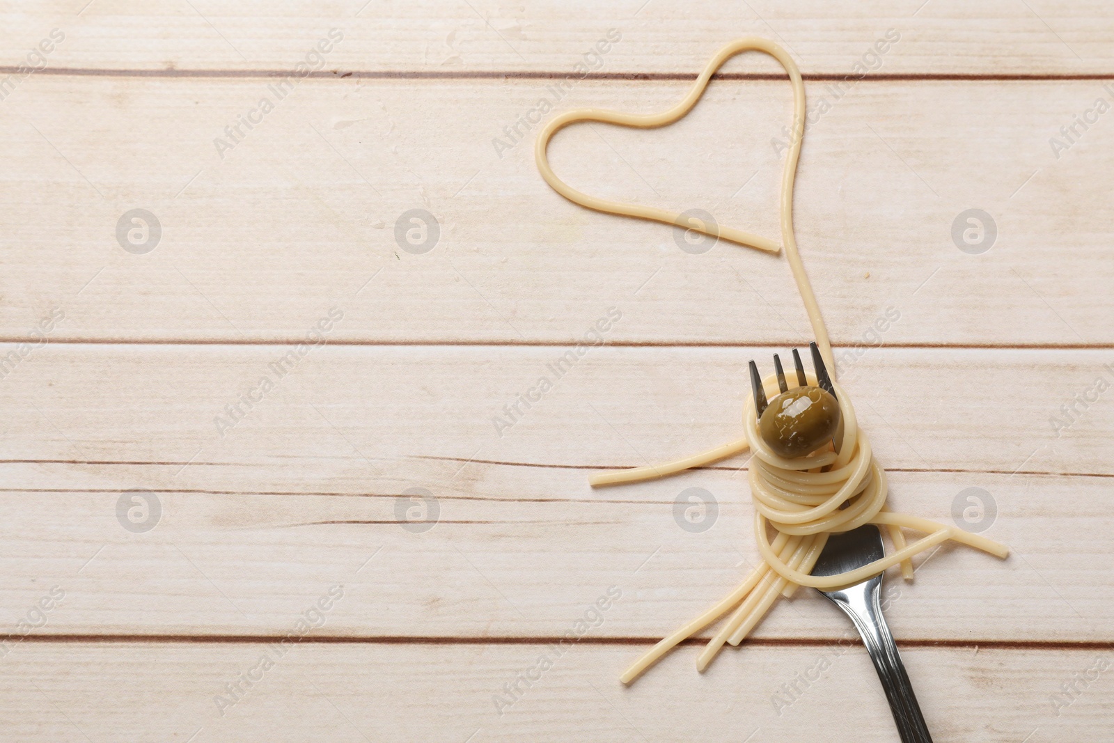 Photo of Heart made of tasty spaghetti, fork and olive on light wooden table, top view. Space for text