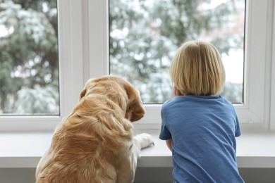 Photo of Cute little child with Golden Retriever near window at home, back view. Adorable pet