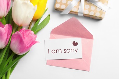 Image of Card with phrase I Am Sorry, pink envelope, bouquet of tulips and gift box on white background, flat lay