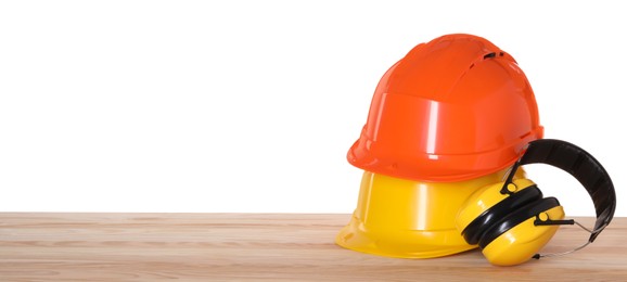 Hard hats and earmuffs on wooden table against white background. Safety equipment