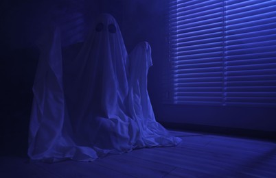 Photo of Creepy ghost. Woman covered with sheet near window in blue light, space for text