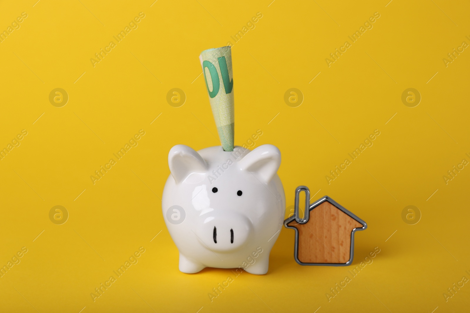 Photo of Ceramic piggy bank, euro banknote and key trinket on yellow background. Financial savings