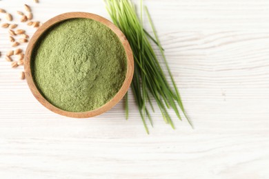 Photo of Wheat grass powder in bowl, seeds and fresh sprouts on white wooden table, flat lay. Space for text