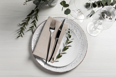 Stylish setting with cutlery and eucalyptus leaves on white wooden table, flat lay