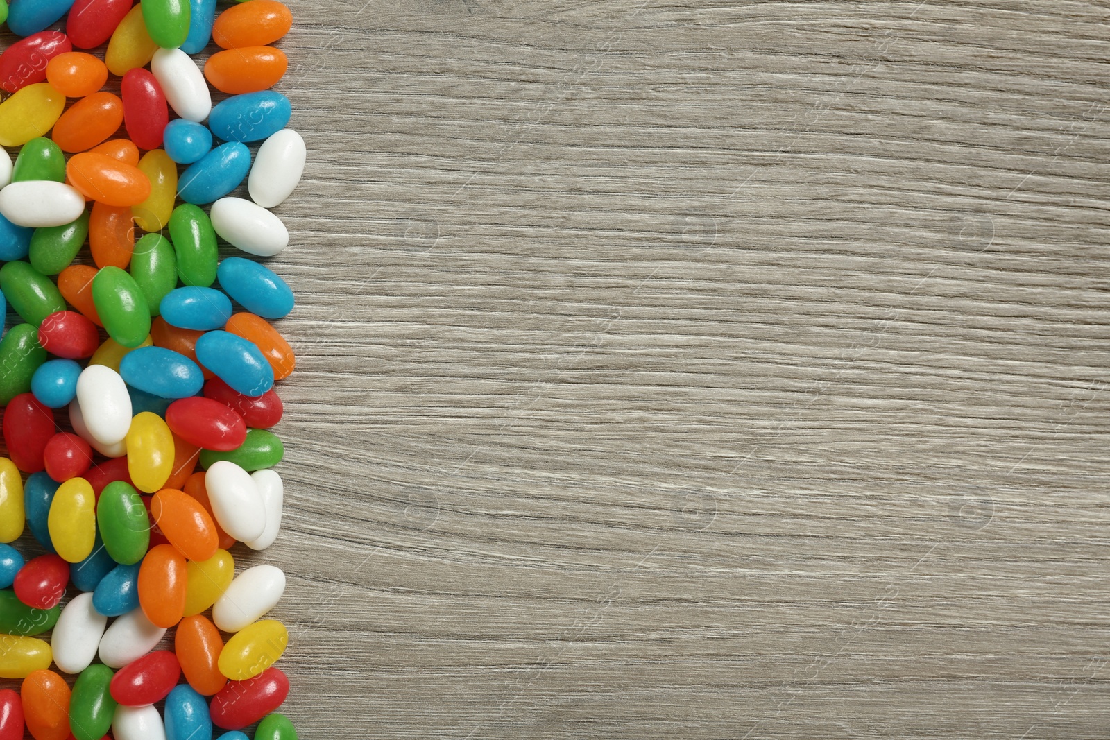 Photo of Delicious bright jelly beans on wooden background, top view. Space for text