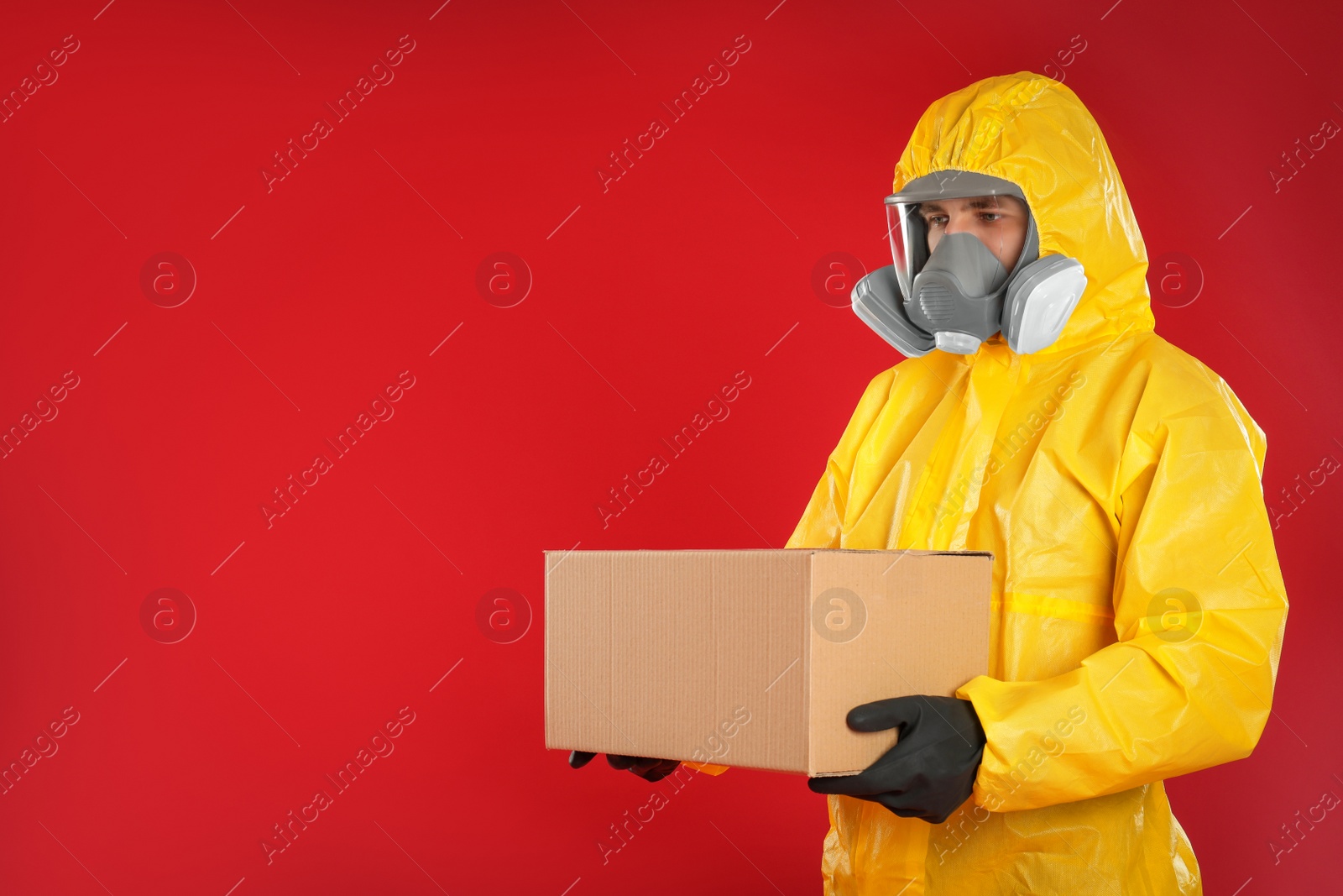 Photo of Man wearing chemical protective suit with cardboard box on red background, space for text. Prevention of virus spread