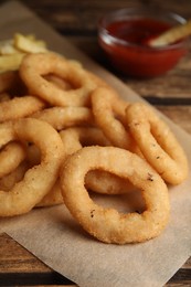 Photo of Delicious onion rings, fries and ketchup on wooden table, closeup