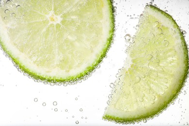 Photo of Juicy lime slices in soda water against white background, closeup