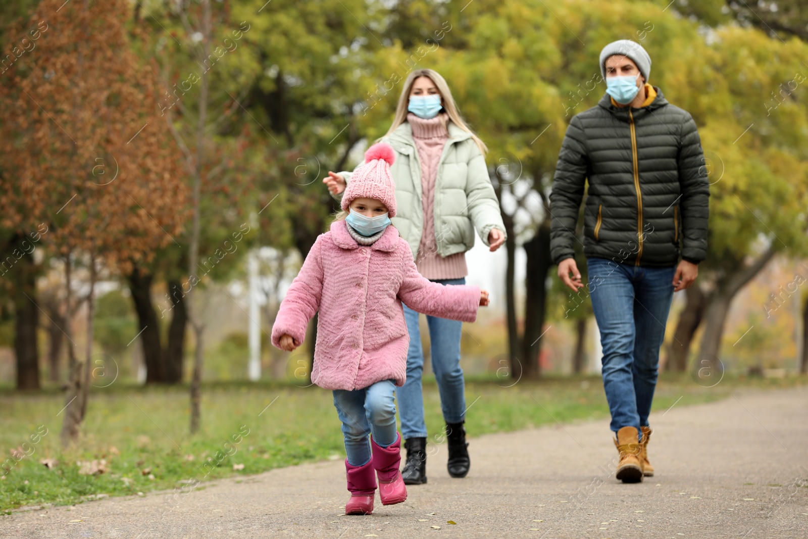 Photo of Family in medical masks walking outdoors on autumn day. Protective measures during coronavirus quarantine