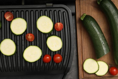 Photo of Electric grill with vegetables on black table, flat lay