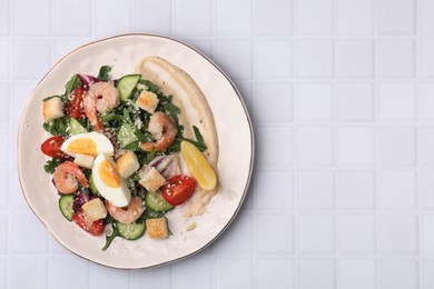 Photo of Delicious Caesar salad with shrimps on white tiled table, top view. Space for text