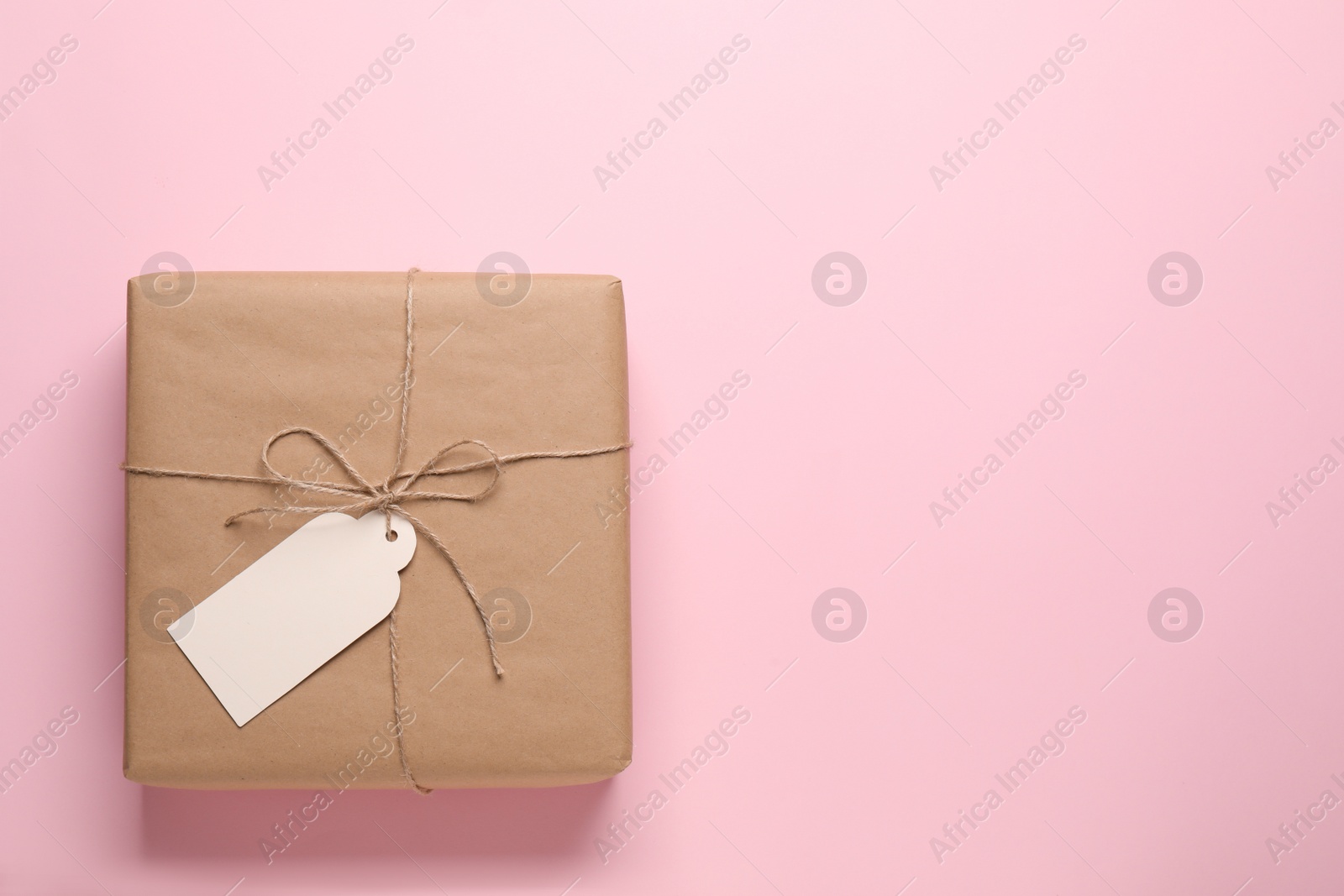 Photo of Parcel wrapped in kraft paper with tag on pink background, top view. Space for text