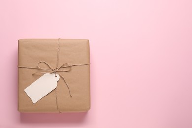 Parcel wrapped in kraft paper with tag on pink background, top view. Space for text