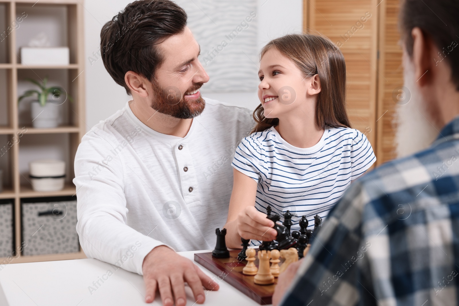 Photo of Family playing chess together at table in room