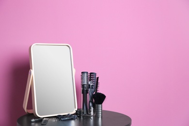 Photo of Stylish mirror and hairdressing accessories on table near color wall