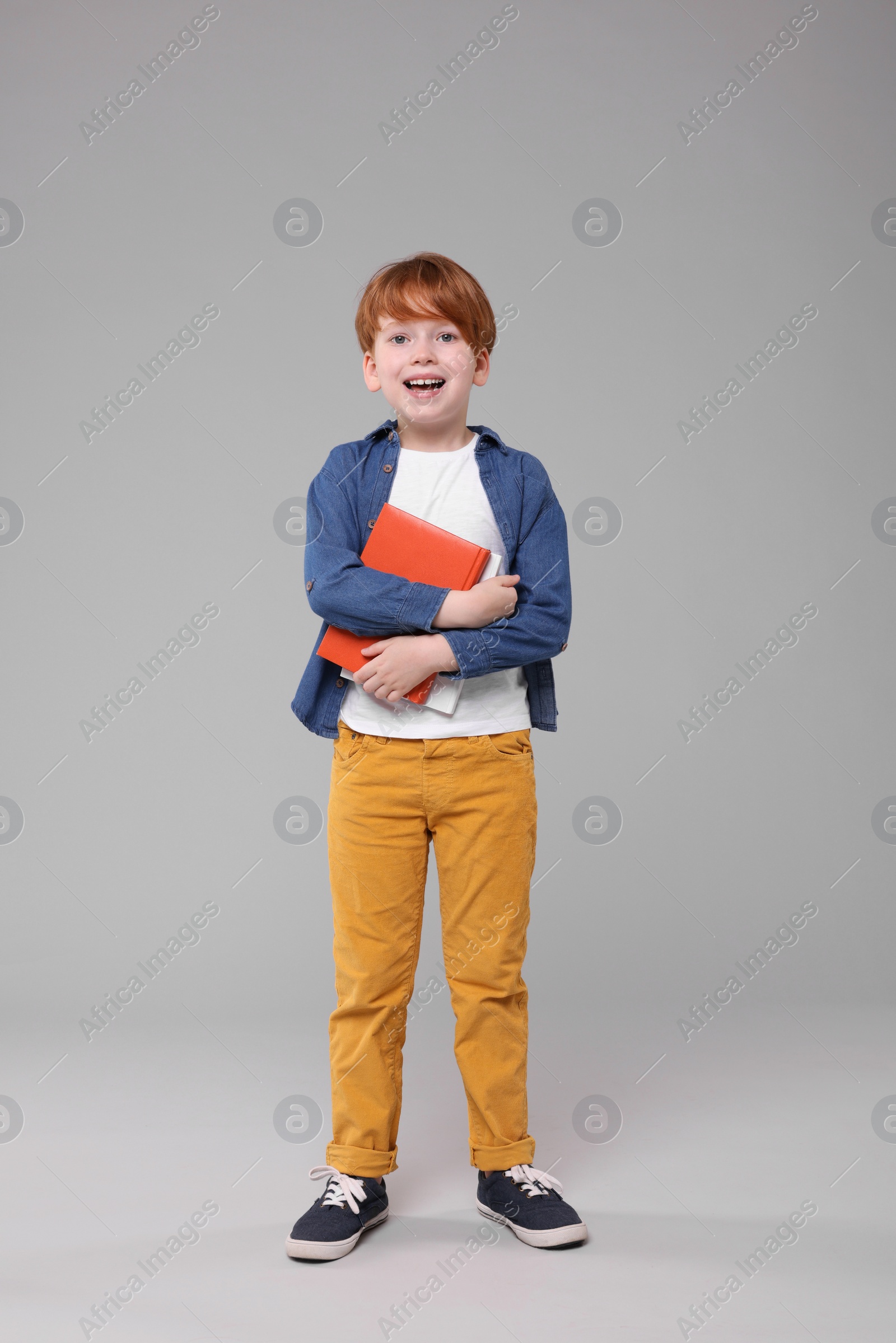 Photo of Happy schoolboy with books on grey background