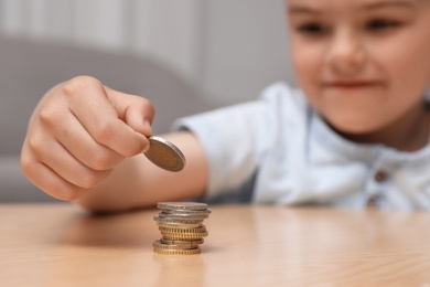 Photo of Cute little boy stacking coins at home, focus on hand