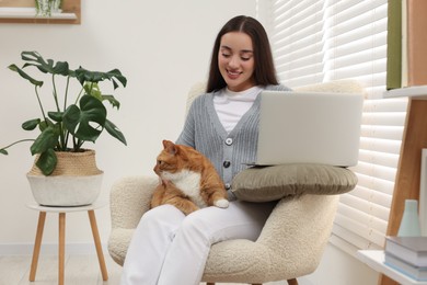 Happy woman working with laptop and petting cute cat at home