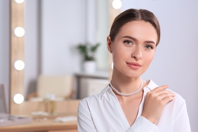 Photo of Young woman wearing elegant pearl necklace indoors, space for text