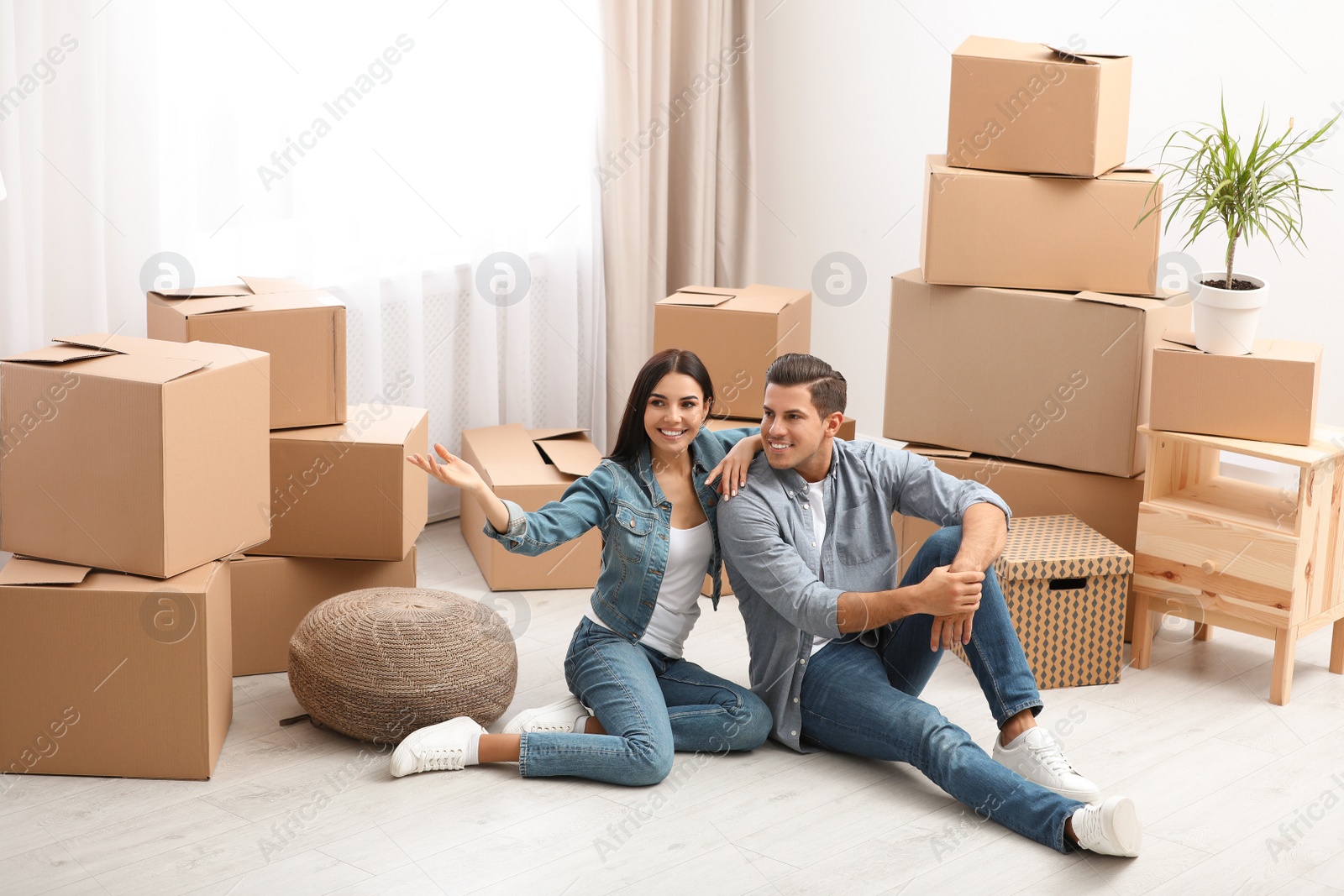 Photo of Happy couple in room with cardboard boxes on moving day