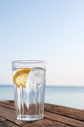 Photo of Wooden table with glass of refreshing lemon drink on hot summer day outdoors, space for text