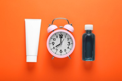 Container with toothpaste, alarm clock and bottle of mouthwash on orange background, flat lay
