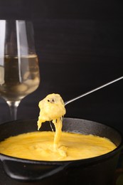 Dipping piece of bread into fondue pot with melted cheese on table, closeup