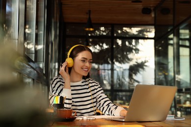 Photo of Young female student with laptop and headphones studying at table in cafe