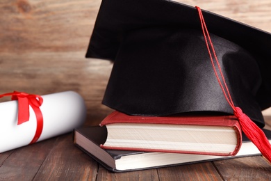 Photo of Graduation hat, books and student's diploma on wooden table, closeup