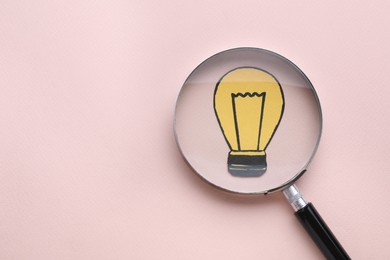 Magnifying glass over paper light bulb on pink background, top view. Space for text