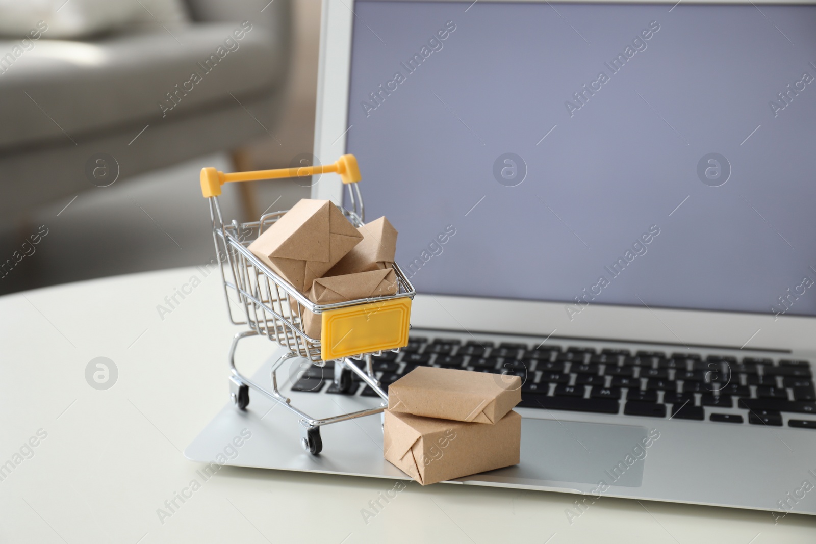 Photo of Internet shopping. Laptop and small cart with boxes on table indoors