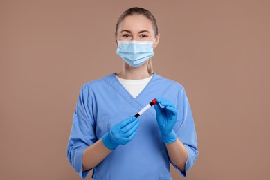Laboratory testing. Doctor with blood sample in tube on light brown background