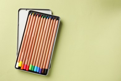 Photo of Box with many colorful pastel pencils on light olive background, top view and space for text. Drawing supplies