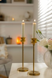 Photo of Pair of beautiful golden candlesticks on white table in room