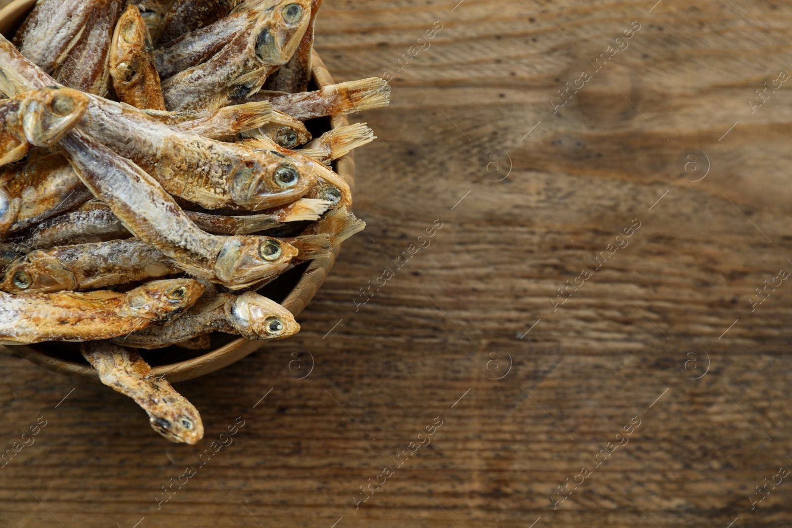 Photo of Delicious dried anchovies on wooden table. Space for text