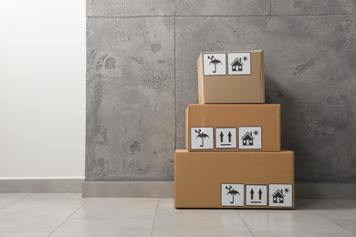 Photo of Many closed cardboard boxes with packaging symbols on floor indoors, space for text. Delivery service