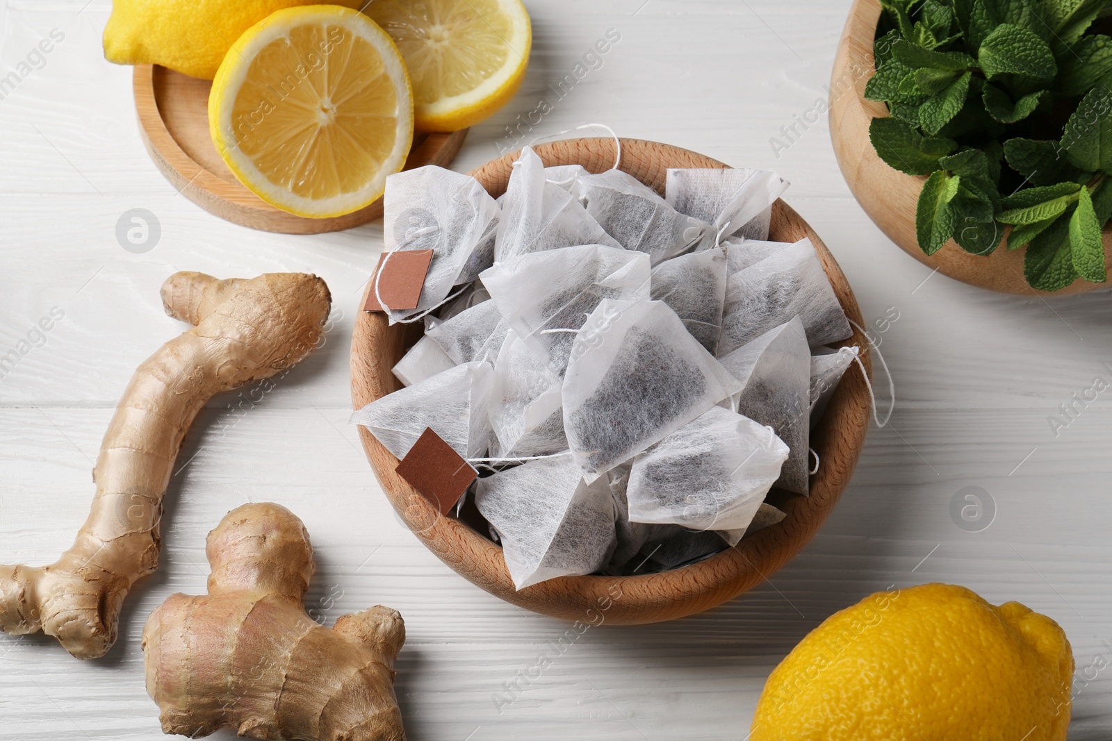 Photo of Tea bags, mint, lemons and ginger on white wooden table, above view