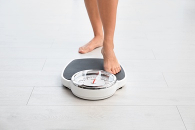 Photo of Woman standing on scales indoors. Overweight problem
