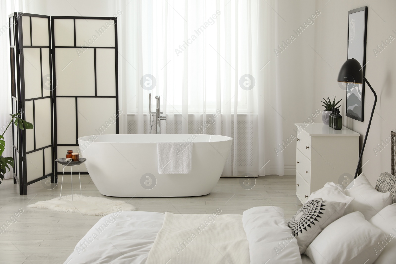Photo of Stylish light apartment interior with white bathtub and bed