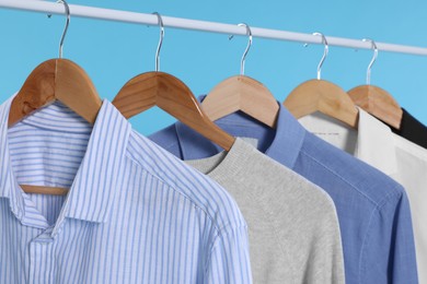 Rack with stylish clothes on wooden hangers against light blue background, closeup