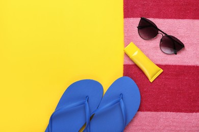 Photo of Flip flops, sunscreen, stylish sunglasses and striped towel on yellow background, flat lay. Space for text