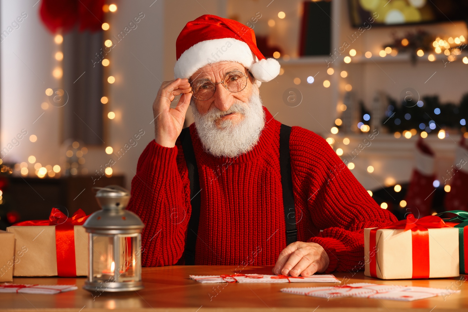 Photo of Santa Claus at his workplace. Letters and gift boxes on table in room with Christmas tree