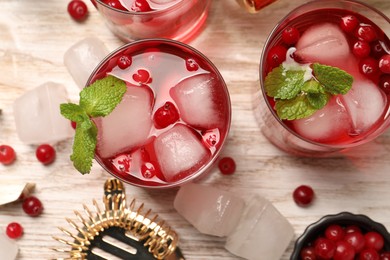 Photo of Tasty cranberry cocktail with ice cubes and mint in glasses on wooden table, flat lay