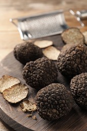 Photo of Whole and cut black truffles with wooden board on table