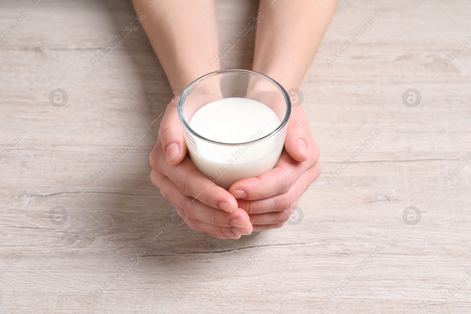 Photo of Woman holding glass of milk at white wooden table, closeup