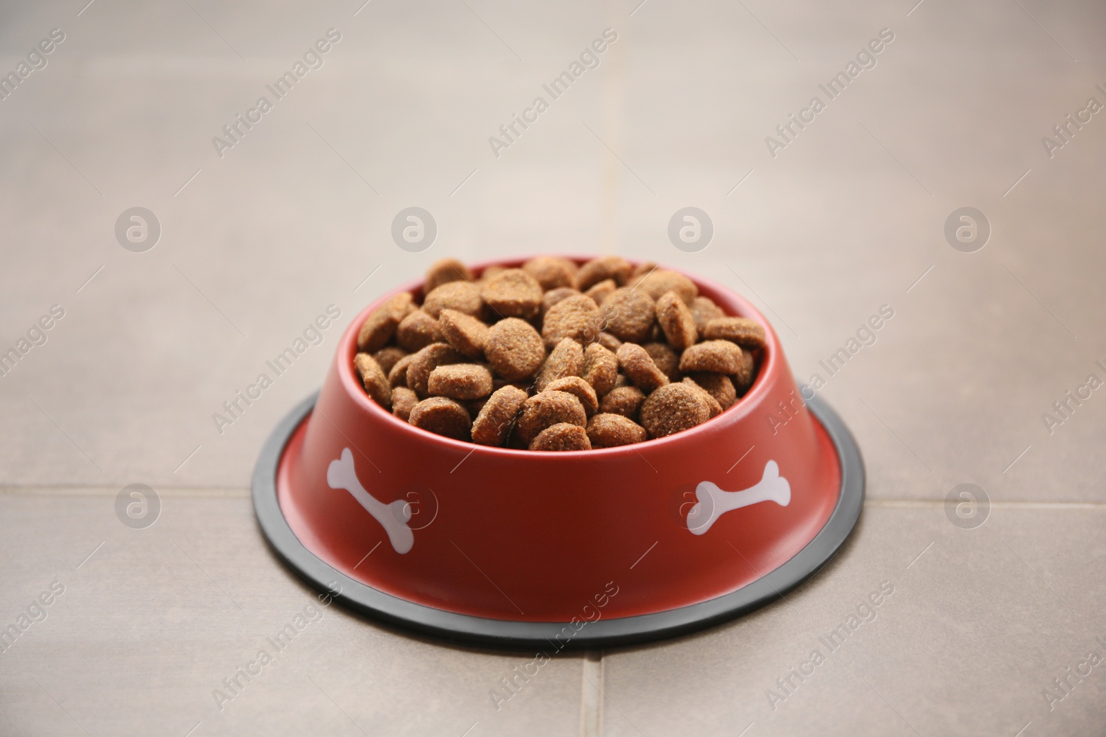 Photo of Dry dog food in feeding bowl on tiled floor