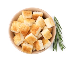 Delicious crispy croutons in bowl and rosemary on white background, top view
