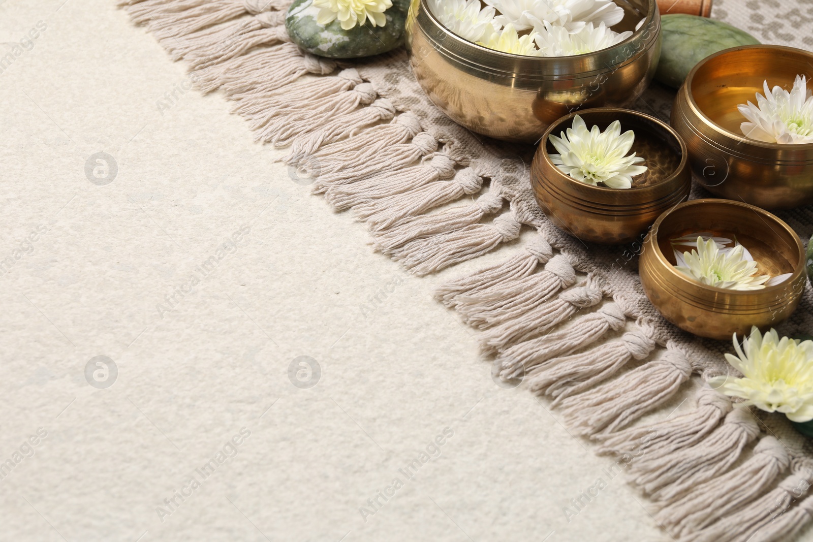 Photo of Tibetan singing bowls with water and beautiful chrysanthemum flowers on beige table, space for text