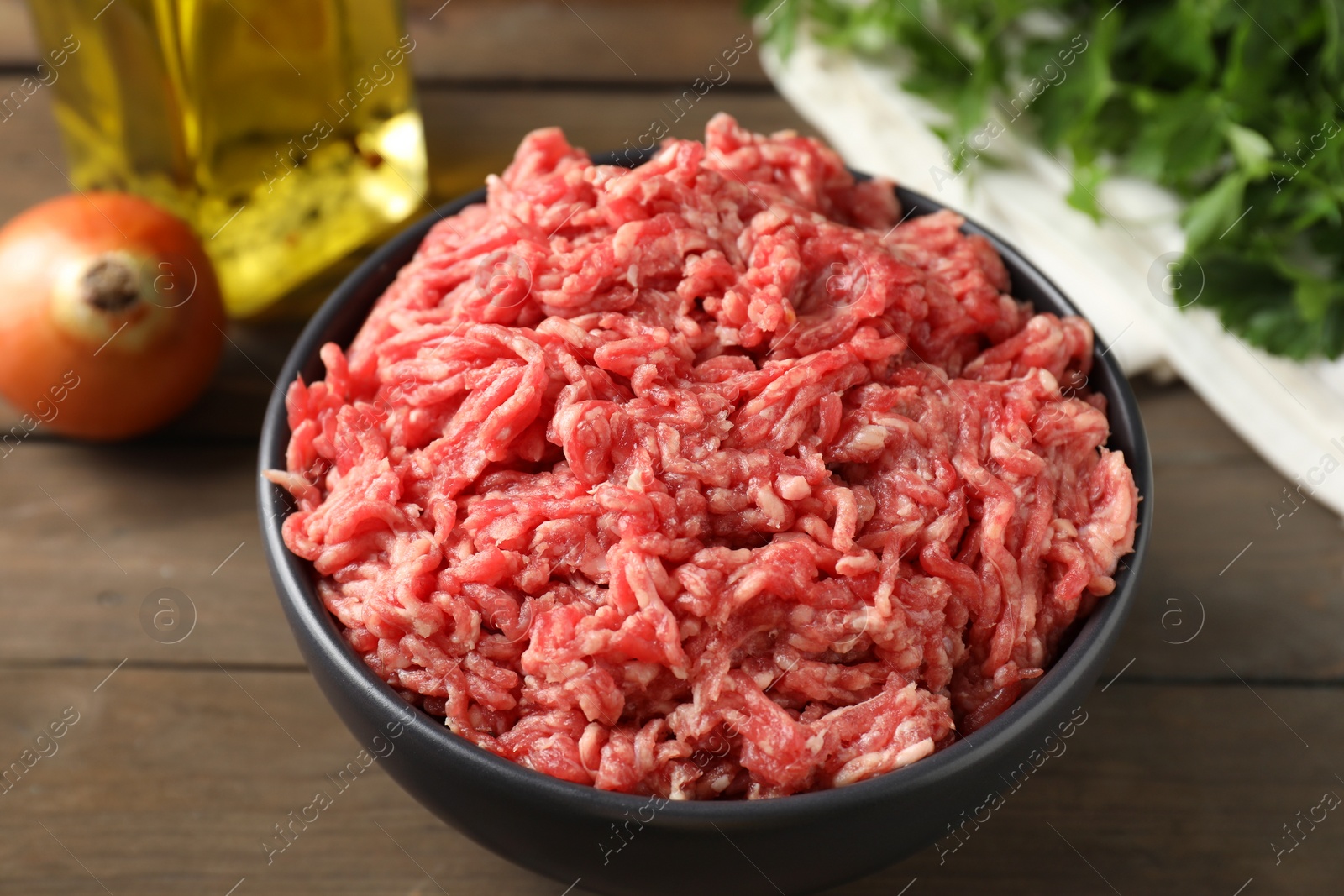 Photo of Raw ground meat in bowl on wooden table, closeup