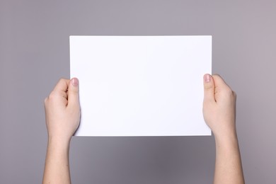 Photo of Woman holding sheet of paper on grey background, closeup. Mockup for design